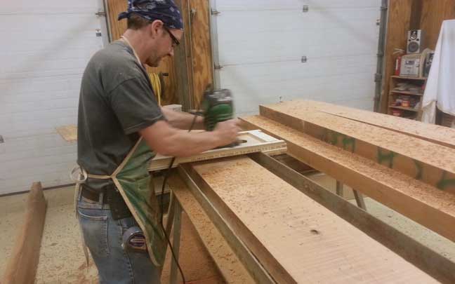 Tom Bloxham, lead artisan at Silent Rivers, planes and distresses large planks of cherry wood for custom designed table for 12