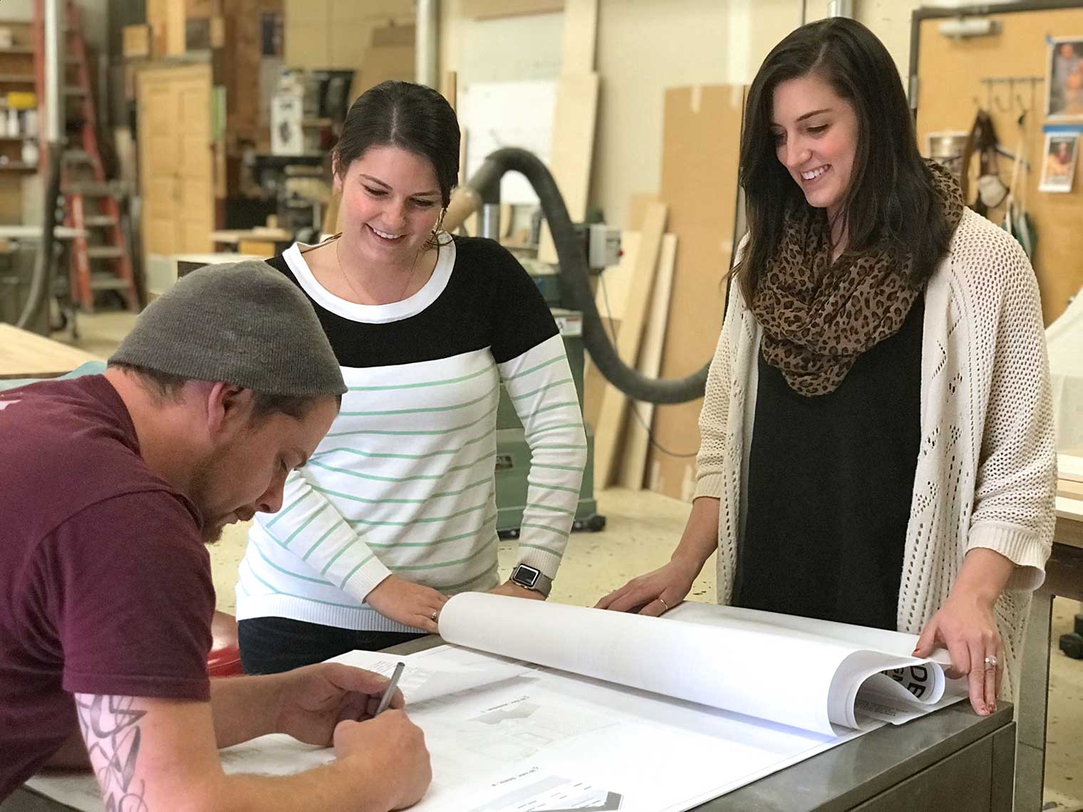 new design assistants Caitlin Cuevas and Amie Schurman review architectural plans with woodshop artisan Alex Schlepphorst.